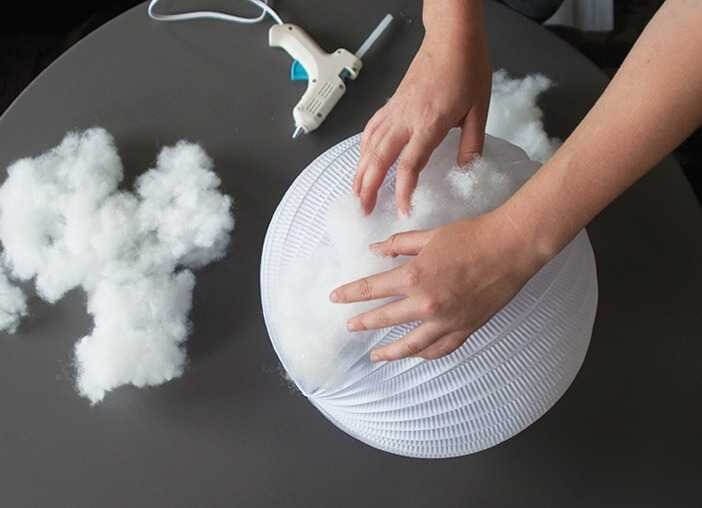 Người đang nhồi bông vào đèn lồng giấy tròn cạnh súng bắn keo trên bàn màu đen, tạo sản phẩm thủ công DIY.