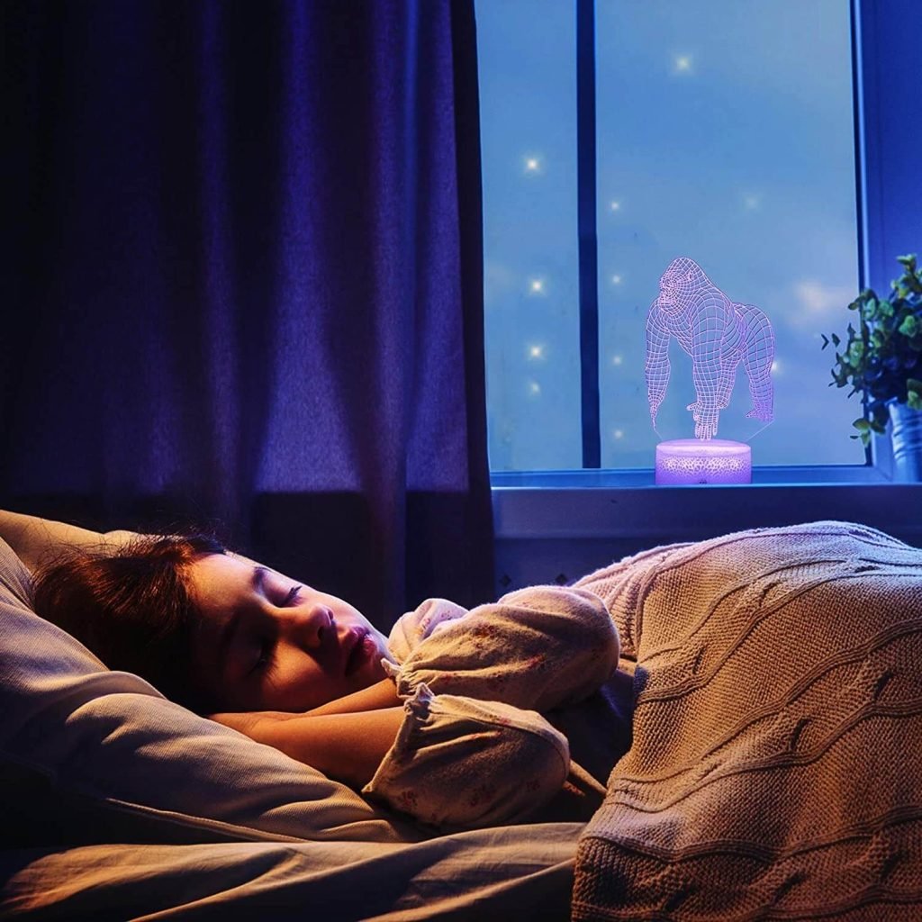 Bé gái ngủ ngon bên cửa sổ với đèn LED 3D hình khỉ đột phát sáng màu tím trong phòng tạo cảm giác yên bình.
