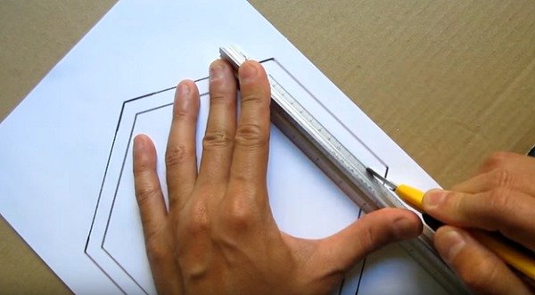 Người dùng vẽ một hình lục giác trên giấy trắng bằng thước kim loại và dao cắt trên bề mặt bìa cứng.