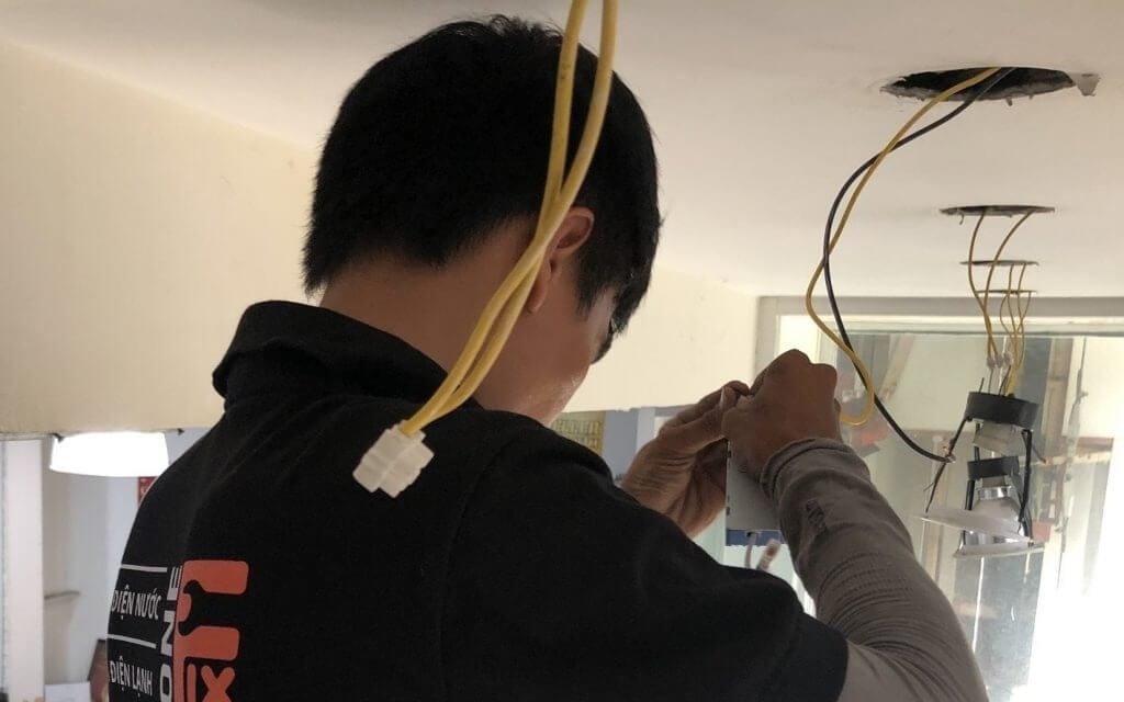 Kỹ thuật viên lắp đặt hệ thống điện trên trần nhà, tập trung và tỉ mỉ điều chỉnh dây dẫn cho an toàn.