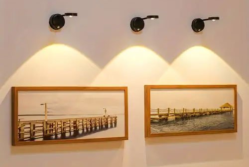 Hai bức tranh cầu tàu gỗ treo trên tường, được chiếu sáng bởi ba đèn gắn tường và khung gỗ tự nhiên.