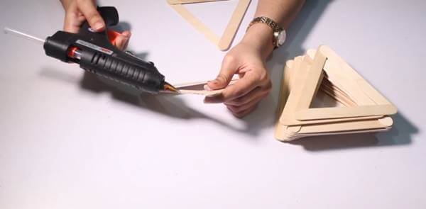 Người đang sử dụng súng bắn keo để dán các que kem thành hình tam giác cho dự án thủ công DIY.