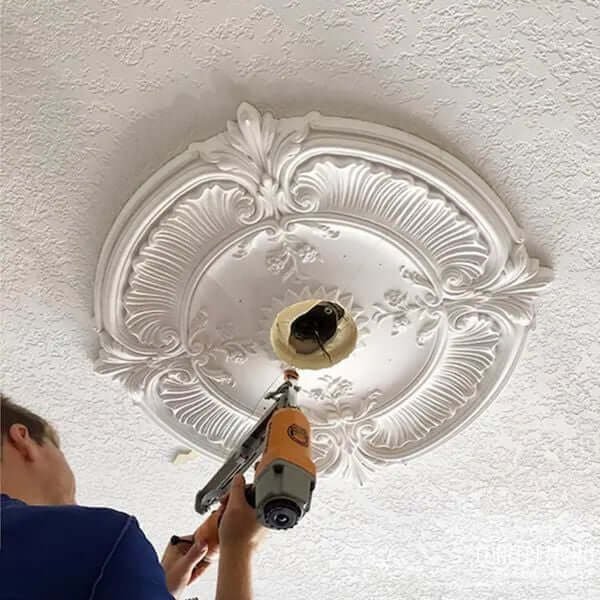 Người thợ lắp đặt mâm vòm trang trí trần nhà bằng súng bắn đinh, với hoa văn tinh xảo và chi tiết nghệ thuật.