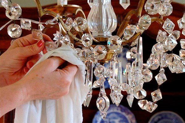 Người đang lau chùi đèn chùm pha lê, giữ cho đèn sáng bóng và sạch sẽ với khăn trắng trong phòng khách.