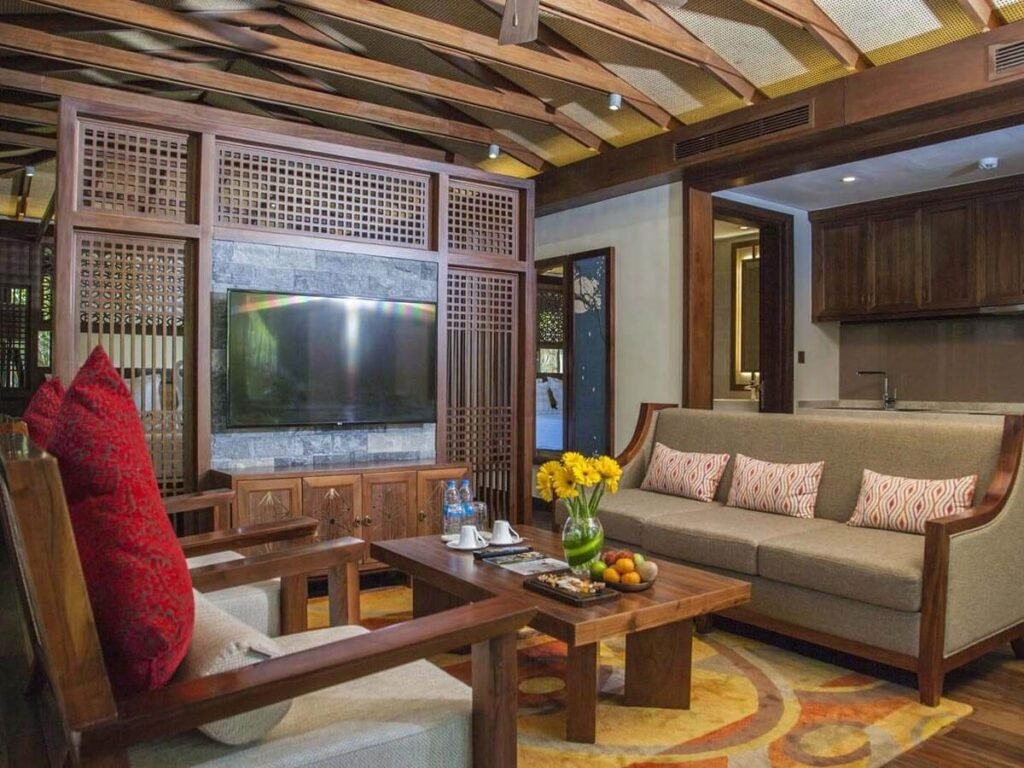 45 mẫu vách ngăn trang trí phòng khách tuyệt đẹp ấm cúng với ghế sofa, gối đỏ, bàn trà gỗ, tivi treo tường và trang trí hoa tươi sáng.