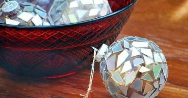 tái chế đồ cũ để trang trí phòng bằng quả cầu trang trí Giáng Sinh với gương ghép lấp lánh bên cạnh bát thủy tinh màu đỏ trên mặt bàn gỗ.